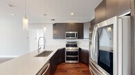 This well-designed 3-bedroom, 1-bathroom single-floor unit offers a thoughtful open-concept layout that maximizes its compact footprint. Rich hardwood flooring flows consistently throughout, lending warmth and cohesion to every room.

The kitchen is a standout, outfitted with dark espresso cabinetry, quartz countertops, stainless steel appliances including a double oven range, built-in microwave, and French door refrigerator. A large island with an undermount sink and elegant pendant lighting anchors the space, seamlessly connecting the kitchen to the living area.

The open living area benefits from large windows that frame urban city views, filling the space with natural light. The primary bedroom is generously proportioned, featuring city-facing windows and its own ceiling fan. The additional bedrooms are well-sized, each with hardwood floors, ceiling fans, and ample closet space including louvered sliding doors.

The bathroom is a refined retreat, highlighted by a glass-enclosed walk-in shower clad floor-to-ceiling in marble-look tile with built-in corner shelving and a modern multi-function shower system. The overall aesthetic is clean and contemporary, with a neutral grey and white palette that creates a bright, airy ambiance throughout.