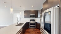 This well-designed 3-bedroom, 1-bathroom single-floor unit offers a thoughtful open-concept layout that maximizes its compact footprint. Rich hardwood flooring flows consistently throughout, lending warmth and cohesion to every room.

The kitchen is a standout, outfitted with dark espresso cabinetry, quartz countertops, stainless steel appliances including a double oven range, built-in microwave, and French door refrigerator. A large island with an undermount sink and elegant pendant lighting anchors the space, seamlessly connecting the kitchen to the living area.

The open living area benefits from large windows that frame urban city views, filling the space with natural light. The primary bedroom is generously proportioned, featuring city-facing windows and its own ceiling fan. The additional bedrooms are well-sized, each with hardwood floors, ceiling fans, and ample closet space including louvered sliding doors.

The bathroom is a refined retreat, highlighted by a glass-enclosed walk-in shower clad floor-to-ceiling in marble-look tile with built-in corner shelving and a modern multi-function shower system. The overall aesthetic is clean and contemporary, with a neutral grey and white palette that creates a bright, airy ambiance throughout.