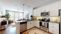 This single-floor residence is thoughtfully designed with a cohesive, modern aesthetic that balances functionality and comfort. The entry opens directly into the kitchen and living area, establishing an open-concept layout that promotes a sense of spaciousness. The kitchen is well-appointed with white shaker-style cabinetry, dark countertops, a classic subway tile backsplash, and a full suite of stainless steel appliances including a refrigerator, range, microwave, and dishwasher. A peninsula with an undermount sink and globe pendant lighting above serves as a natural divider between the kitchen and the adjacent living area. Wood-tone flooring runs throughout the main living spaces, adding warmth and continuity.

The living room benefits from large French doors and windows that allow generous natural light to fill the room, creating a bright and inviting atmosphere. The space comfortably accommodates seating and opens to the outdoors.

The bedrooms are carpeted for comfort and each receives natural light through well-positioned windows. One bedroom features direct access to the hallway and additional storage. The bathroom includes white cabinetry, dark countertops, a tiled shower, and wood-tone flooring, maintaining the consistent design language found throughout the residence.