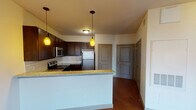 Located at 600 Franklin Ave in Waco, Texas, this single-floor residence offers a thoughtfully designed layout with functional living spaces throughout. The kitchen is a standout feature, showcasing rich dark wood cabinetry, granite-style countertops, a white subway tile backsplash, and a full suite of stainless steel appliances including a range, microwave, and refrigerator. Warm pendant lighting illuminates the peninsula, which provides additional prep space and separates the kitchen from the open living area. The living space features durable hardwood-style flooring that flows seamlessly from the kitchen through the main corridor. The bedroom is carpeted for comfort and includes a window with views of the surrounding downtown Waco streetscape, allowing natural light to fill the room. A generously sized walk-in closet with wire shelving offers ample storage. The bathroom features hardwood-style flooring, a dark-cabineted vanity with a granite-style countertop, a wall-mounted mirror, and stylish sconce lighting. Interior doors are finished in a warm taupe tone, complementing the neutral wall palette throughout. The unit is located in the heart of downtown Waco, providing convenient access to the city's amenities.