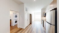 Located at 220 N Walton Blvd in Bentonville, AR, this thoughtfully designed one-bedroom, one-bathroom unit offers a modern living experience within a compact, efficient floor plan. Light-toned wood-look flooring runs throughout, complementing the crisp white walls and creating a bright, cohesive aesthetic.

The kitchen is a standout feature, outfitted with flat-front cabinetry in a warm taupe finish, dark countertops, a subway tile backsplash, and a full suite of stainless steel appliances including a range, over-the-range microwave, dishwasher, and refrigerator. The layout allows for easy flow into the main living area, which receives natural light through a large window.

The hallway connects the living spaces efficiently and reveals a convenient in-unit stacked washer and dryer tucked neatly into a dedicated closet. Additional storage is accessible via closet doors along the hall.

The bedroom is a comfortable, well-proportioned retreat with the same warm wood-look flooring, white walls, and a window fitted with blinds for privacy and light control.

The bathroom features a full soaking tub and shower combination with white subway tile surround and built-in shelving, matte black fixtures and hardware, a wood-toned vanity with a dark countertop, and wood-look flooring that ties the space together. The overall ambiance is clean, modern, and move-in ready.