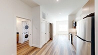 Located at 220 N Walton Blvd in Bentonville, AR, this thoughtfully designed one-bedroom, one-bathroom unit offers a modern living experience within a compact, efficient floor plan. Light-toned wood-look flooring runs throughout, complementing the crisp white walls and creating a bright, cohesive aesthetic.

The kitchen is a standout feature, outfitted with flat-front cabinetry in a warm taupe finish, dark countertops, a subway tile backsplash, and a full suite of stainless steel appliances including a range, over-the-range microwave, dishwasher, and refrigerator. The layout allows for easy flow into the main living area, which receives natural light through a large window.

The hallway connects the living spaces efficiently and reveals a convenient in-unit stacked washer and dryer tucked neatly into a dedicated closet. Additional storage is accessible via closet doors along the hall.

The bedroom is a comfortable, well-proportioned retreat with the same warm wood-look flooring, white walls, and a window fitted with blinds for privacy and light control.

The bathroom features a full soaking tub and shower combination with white subway tile surround and built-in shelving, matte black fixtures and hardware, a wood-toned vanity with a dark countertop, and wood-look flooring that ties the space together. The overall ambiance is clean, modern, and move-in ready.