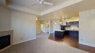 This single-floor residence offers a thoughtfully designed open-concept layout that seamlessly connects the living area and kitchen. The spacious living room features a tray ceiling with a ceiling fan, plush carpeting, and a tile-surround fireplace flanked by large windows that invite ample natural light and outdoor views of surrounding trees. The kitchen is well-equipped with dark espresso cabinetry, light countertops, a full suite of black appliances including a refrigerator, range, microwave, and dishwasher, as well as a central island with pendant lighting and rich hardwood-style flooring. Track lighting overhead adds functional illumination throughout the cooking area. The bedrooms are carpeted and each include ceiling fans and windows, providing comfort and natural light. Two bathrooms serve the unit: one featuring a full tub-shower combo with white tile surround and dark vanity cabinetry, and a second with a standalone vanity and hardwood-style flooring. A dedicated utility room houses an in-unit washer and water heater, adding everyday convenience. The warm, neutral color palette throughout creates a cohesive and welcoming ambiance suited for comfortable everyday living.