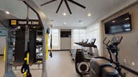 Located on Meehan Street in Santa Maria, California, this well-equipped fitness center offers a comprehensive workout environment within a thoughtfully designed single-floor space. The facility is bathed in natural light courtesy of large, floor-to-ceiling windows fitted with roller shades, providing a bright and energizing atmosphere throughout.

The cardio zone features a row of Life Fitness treadmills and elliptical trainers positioned to take advantage of the natural light and exterior views. Wall-mounted flat-screen televisions are strategically placed throughout, allowing users to stay entertained during their workouts. Overhead, large statement ceiling fans with bold blade spans provide both airflow and a modern industrial aesthetic, complemented by recessed lighting.

The strength training area is equally well-appointed, featuring a dedicated free weight section with a full rack of dumbbells, a weight bench, and plate-loaded equipment. A functional training zone includes a multi-station cable machine and TRX suspension training system. Stability balls and kettlebells are neatly organized on a multi-tiered storage rack.

Full-length framed mirrors line key sections of the walls, enhancing the sense of space and allowing users to monitor their form. A built-in water bottle filling station adds a practical, modern convenience. The durable, light-toned flooring ties the clean, neutral color palette together, creating a professional and motivating fitness environment.