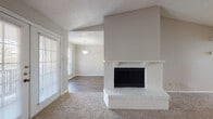 Located at 11710 Parliament St in San Antonio, Texas, this single-floor residence offers a well-organized layout with a variety of functional spaces. The living room serves as the centerpiece, highlighted by a striking white brick fireplace with a raised hearth and a classic mantle. Vaulted ceilings lend a sense of openness and volume to the space, while plush carpeting adds warmth underfoot. A set of French doors opens to a private balcony, allowing natural light to flow freely into the room. Adjacent to the living area, a separate dining space features wood-look flooring and an elegant pendant light fixture, creating a distinct and inviting atmosphere. The galley-style kitchen is efficiently designed with white cabinetry lining both walls, dark countertops, wood-look flooring, and white appliances including a range, microwave, and refrigerator. A pantry closet adds to the kitchen's storage capacity. The bathroom features wood-look flooring, a tiled tub-shower combo, and a countertop with integrated sink. The carpeted bedroom benefits from a large window that frames views of surrounding greenery, filling the room with soft, natural light. A textured ceiling is consistent throughout the home, contributing to its cohesive character.