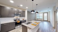 This well-appointed one-bedroom, one-bathroom residence offers a thoughtfully designed open-concept layout that maximizes its efficiently used single-floor footprint. The kitchen serves as the centerpiece of the living area, showcasing dark espresso cabinetry, a classic white subway tile backsplash, granite countertops, and a large center island with an undermount sink — all illuminated by stylish pendant lighting. Stainless steel appliances, including a side-by-side refrigerator with ice dispenser, electric range, and built-in microwave, complete the modern kitchen ensemble. The kitchen flows seamlessly into the living area, which benefits from natural light streaming through large windows fitted with horizontal blinds. Wood-look luxury vinyl plank flooring runs throughout the main living spaces, lending warmth and visual continuity. The bedroom is a comfortable, carpeted retreat with neutral tones and ample wall space. The bathroom features a granite-topped vanity with an undermount sink, a glass-enclosed shower, and wood-look tile flooring. A dedicated closet with built-in organization is conveniently accessible directly from the bathroom, providing practical everyday storage. A ceiling fan in the living area adds to the overall comfort of this clean, contemporary residence.