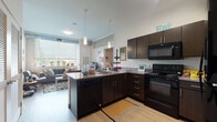 Located at 1750 Euclid Ave in the heart of Cleveland, Ohio, this modern single-floor residential unit offers a well-designed open layout with contemporary finishes throughout. The kitchen serves as a central hub of the living space, featuring dark espresso cabinetry, granite-style countertops, black appliances including a range, over-the-range microwave, and dishwasher, along with a peninsula with bar seating — ideal for casual dining and entertaining. The kitchen flows seamlessly into the living area, which benefits from large windows that invite generous natural light and offer views of the surrounding urban landscape, including the nearby Cleveland State University campus. Exposed ductwork along the ceiling adds an industrial design element that complements the unit's modern aesthetic. The bedroom is a comfortable, well-lit retreat featuring large windows with outdoor views, carpeted flooring, and a built-in shelf for added storage. An adjacent closet provides convenient access to the full bathroom, which is outfitted with dark wood vanity cabinetry, a large mirror, and a shower-tub combination. Wood-style flooring in the main living areas and tile in the bathroom round out the clean, functional design of this urban residence.