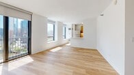 Located at 520 N Kingsbury Street in Chicago's River North neighborhood, this efficiently designed studio offers a clean, modern aesthetic throughout its single-floor layout. The open-plan kitchen and living area forms the heart of the space, bathed in natural light streaming through large floor-to-ceiling sliding glass doors and expansive windows that frame views of the Chicago skyline. Light hardwood flooring runs throughout the main living area, lending warmth to the bright white walls and contemporary finishes.

The galley-style kitchen is thoughtfully appointed with warm-toned wood cabinetry, white quartz countertops, a subway tile backsplash, and a full suite of stainless steel appliances including a refrigerator, range, microwave, and dishwasher. A pass-through opening connects the kitchen to the living area, enhancing the sense of openness.

The bathroom features neutral tile flooring, a wood-grain vanity with a white countertop, a large wall mirror, and chrome accents, maintaining the unit's clean and modern character. A dedicated closet provides practical storage. The entry hallway, with light tile flooring, leads seamlessly into the main living space. Overall, the unit presents a bright, minimalist atmosphere well-suited to urban living in one of Chicago's most vibrant neighborhoods.