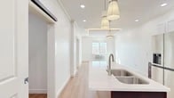This thoughtfully designed one-bedroom, one-bathroom residence at 523 Wheelers Farms Rd in Milford, CT offers a clean, modern aesthetic throughout. Light hardwood flooring flows seamlessly across the entire floor plan, complementing the bright white walls and recessed lighting that give every room an airy, open feel.

The combined kitchen and living area serves as the heart of the home, anchored by a striking kitchen featuring a central island with a white quartz countertop, rich dark cabinetry on the lower level, crisp white upper cabinets, a subway tile backsplash, and stainless steel appliances including a refrigerator, stove, and dishwasher. Pendant lighting adds a stylish focal point overhead. A stacked in-unit washer and dryer is conveniently tucked just off the kitchen.

The bedroom is comfortably sized, filled with natural light from large windows that frame views of the surrounding neighborhood. The room also features crown molding and a wall-mounted HVAC unit for year-round comfort. Two closets provide generous storage throughout the unit.

The bathroom is a standout, finished with large-format marble-look porcelain tile on both the floors and the walk-in shower walls. A frameless sliding glass shower door and built-in shelving complete this elegant space. The hallway connects all rooms efficiently, maximizing the well-utilized layout of this polished residence.
