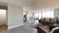 This single-floor unit offers a thoughtfully designed open-concept layout that seamlessly connects the living, dining, and kitchen areas. The living room is a welcoming space featuring light wood-tone flooring, a textured ceiling, and large floor-to-ceiling windows that flood the interior with natural light and frame sweeping panoramic views of the surrounding landscape. A sliding glass door provides direct access to a private balcony, ideal for taking in the scenery.

The kitchen is outfitted with crisp white shaker-style cabinetry, light stone countertops, and a full suite of stainless steel appliances, including a range, microwave, dishwasher, and refrigerator. A peninsula with bar seating connects the kitchen to the dining area, creating a practical and social layout.

The bedroom is a calm, carpeted retreat with neutral tones and ample space for furnishings. The bathroom features a clean, contemporary design with a white shaker vanity, white quartz countertop, large-format tile flooring, and a tiled tub-shower combination.

Throughout the unit, consistent light wood-tone flooring, neutral wall colors, and modern finishes create a cohesive and polished aesthetic that is both functional and inviting.