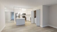 This thoughtfully renovated single-floor residence offers a clean, contemporary aesthetic defined by bright white tones, light wood-look flooring, and a seamless open layout. The kitchen serves as a focal point of the home, showcasing crisp white shaker cabinetry extending to the ceiling, quartz countertops, and a full suite of stainless steel appliances including a refrigerator, electric range, microwave, and dishwasher. A central island provides additional prep and gathering space, while pendant lighting and a flush ceiling fixture illuminate the area warmly. Conveniently tucked just off the kitchen is an in-unit laundry area with a washer and dryer. The living areas feature light-toned plank flooring and large windows dressed with vertical blinds, allowing natural light to fill the space generously. The bedroom is carpeted and includes a wall-unit HVAC system and a window with outdoor views. Two bathrooms complete the unit, both finished with elegant marble-style tile. One bathroom features a soaking tub with shower combination, while the second offers a walk-in glass-enclosed shower — both appointed with white vanities and coordinating fixtures for a polished, cohesive feel throughout.