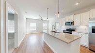 This well-appointed single-story home in La Porte, Texas offers a thoughtfully designed layout with four bedrooms, three bathrooms, and a dedicated laundry room. The open-concept kitchen and living area serves as the heart of the home, showcasing a large center island with a quartz countertop, undermount sink, and stylish pendant lighting. Crisp white shaker cabinets, a subway tile backsplash, and stainless steel appliances — including a French door refrigerator with ice maker, electric range, and built-in microwave — complete the kitchen's clean, modern aesthetic. Warm wood-look flooring flows throughout the entire home, adding continuity and a welcoming feel. A charming barn door leads to a mudroom area equipped with built-in shelving and coat hooks, providing a practical entryway transition. The generously sized primary bedroom offers direct access to the outdoors and connects to a well-equipped en suite bathroom featuring dual undermount sinks, quartz countertops, a large mirror, and a walk-in closet with dual hanging rods. Additional closets provide extensive storage, including a pantry with floor-to-ceiling shelving. The home's neutral color palette and recessed lighting create a bright, airy ambiance throughout.