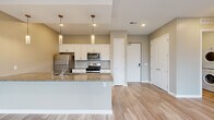 This well-appointed 3-bedroom, 2-bathroom single-floor residence at 5050 Transit Rd in Depew, NY offers a thoughtfully designed open layout. The kitchen is a standout feature, showcasing granite countertops, a peninsula with dual-tone cabinetry—white uppers paired with navy blue lowers—stainless steel appliances including a gas range, microwave, and refrigerator, and elegant pendant lighting overhead. Light wood-look flooring flows throughout the main living areas, creating a clean, cohesive aesthetic. The open-concept design connects the kitchen seamlessly to the living area for easy entertaining. The primary bedroom is generously sized and includes a walk-in closet, while additional bedrooms feature plush carpeting and large windows that invite natural light and offer outdoor views. One bedroom provides direct access to a private balcony with scenic wooded views. The primary bathroom features a glass-enclosed walk-in shower and a granite-topped vanity, while the second bathroom is equipped with a full tub-shower combo. Neutral warm-toned walls throughout lend the space a calm, modern ambiance well-suited for comfortable everyday living.