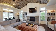 This single-floor clubhouse is a well-appointed gathering space that blends rustic charm with modern sophistication. The centerpiece of the main lounge is a striking stacked-stone fireplace framed by shiplap accent walls and flanked by built-in white bookshelves, with a wall-mounted flat-screen television positioned above. A tufted leather ottoman anchors the seating area, which is complemented by a mix of upholstered chairs and sofas arranged for comfortable socializing. Overhead, a reclaimed wood plank ceiling adds warmth and texture, while a geometric chandelier provides an industrial-inspired accent.

Adjacent to the lounge, a quiet seating nook features a pair of elegant arm chairs positioned beside large windows that frame views of the surrounding greenery, inviting natural light throughout the day. High transom windows further enhance the bright, airy atmosphere across the space.

The clubhouse also includes a stylish kitchen outfitted with deep navy cabinetry, brass hardware, white quartz countertops, a subway tile backsplash, and stainless steel appliances, making it fully functional for events and gatherings. Rich dark hardwood flooring runs throughout, tying all areas together cohesively. A casual bar-height dining area with bistro tables and plaid-upholstered stools lines a window wall, offering an inviting spot for informal conversation or light refreshments.