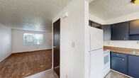 Located at 1250 Kelburn Rd in Columbus, Ohio, this three-floor home offers a practical and functional layout spread across multiple levels. The kitchen is equipped with dark navy cabinetry providing ample upper and lower storage, brown granite-style countertops, a stainless steel double sink, a white electric coil range, and a full-size refrigerator — all set on tile flooring beneath a textured ceiling. Adjacent to the kitchen, the main living area transitions to durable flooring and receives natural light through a window. The carpeted rooms throughout the upper floors feature ceiling fans with integrated lighting, textured ceilings, and windows that bring in natural light and views of surrounding greenery. The full bathroom is fitted with a tub-shower combination, a vanity, and tile flooring, with a window above the tub for natural light. A staircase connects the floors, as seen in the dollhouse view, facilitating easy movement between levels. The basement level offers generous open space with painted concrete floors, painted cinder block walls, exposed ceiling infrastructure, and houses the mechanical systems including a water heater and pressure tank — providing excellent utility and storage potential.
