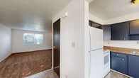 Located at 1250 Kelburn Rd in Columbus, Ohio, this three-floor home offers a practical and functional layout spread across multiple levels. The kitchen is equipped with dark navy cabinetry providing ample upper and lower storage, brown granite-style countertops, a stainless steel double sink, a white electric coil range, and a full-size refrigerator — all set on tile flooring beneath a textured ceiling. Adjacent to the kitchen, the main living area transitions to durable flooring and receives natural light through a window. The carpeted rooms throughout the upper floors feature ceiling fans with integrated lighting, textured ceilings, and windows that bring in natural light and views of surrounding greenery. The full bathroom is fitted with a tub-shower combination, a vanity, and tile flooring, with a window above the tub for natural light. A staircase connects the floors, as seen in the dollhouse view, facilitating easy movement between levels. The basement level offers generous open space with painted concrete floors, painted cinder block walls, exposed ceiling infrastructure, and houses the mechanical systems including a water heater and pressure tank — providing excellent utility and storage potential.