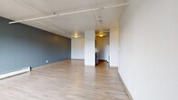 This single-floor unit offers a thoughtfully laid-out living space that balances open-concept design with defined functional areas. The main living area is expansive and open, showcasing light-toned hardwood-style flooring that runs throughout much of the unit. A striking slate-blue accent wall adds depth and character to the space, while exposed conduit and track lighting running along the ceiling lend an industrial aesthetic. Baseboard heating units are positioned along the walls, ensuring year-round comfort. The kitchen is configured as a galley-style layout, lined with dark espresso cabinetry paired with light countertops. It is equipped with a range, refrigerator, dishwasher, and a stainless sink, offering efficient use of space. An adjacent entry area provides two doors and a window, filling the space with natural light and a view of greenery outside. The bedroom features plush carpeting, a window with an outdoor view, and a baseboard heater, creating a warm and comfortable retreat. The bathroom is finished with classic white subway tile surrounding the bathtub and shower, complemented by hardwood-style flooring and a dark vanity. Together, these spaces form a cohesive, modern unit with practical finishes and a clean, contemporary feel.