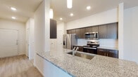 This single-floor residence presents a thoughtfully designed layout with a contemporary aesthetic throughout. The kitchen serves as a central highlight, featuring granite countertops, dark espresso-toned cabinetry with sleek hardware, and a full suite of stainless steel appliances including a refrigerator, electric range, and built-in microwave. A subway tile backsplash adds a clean, modern touch, while pendant lighting and recessed fixtures illuminate the space effectively. A peninsula with an undermount sink provides additional workspace and casual dining potential. Light wood-style flooring runs through the kitchen and extends toward the living area, where a built-in arched shelving niche adds a charming architectural detail.

The bedrooms are carpeted for comfort and each include ceiling fans and windows with blinds that allow natural light and neighborhood views. One bedroom features a sliding glass door opening to a private balcony. The bathrooms are consistent in design, each offering a soaking tub with shower, dark vanity cabinetry, granite countertops, and wood-look tile flooring. The overall palette is neutral and bright, creating a clean, move-in-ready atmosphere throughout.
