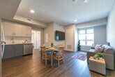 Located at 160 Sherwood Forest Square in London, Ontario, this thoughtfully designed three-bedroom, one-bathroom unit offers a functional and modern living experience across a single floor. The open-concept living and dining area serves as the heart of the home, featuring warm hardwood-style flooring, neutral grey walls, and recessed lighting. A wall-mounted television anchors the living space, while a dining table for four sits adjacent, creating a seamless flow ideal for everyday living. Natural light filters in through a window overlooking the surrounding neighbourhood, adding brightness to the shared space. The kitchen is well-appointed with two-tone grey and white cabinetry, white tile backsplash, light countertops, and a full suite of stainless steel appliances including a refrigerator, electric range, over-the-range microwave, and dishwasher. Each of the three bedrooms features hardwood-style flooring, large windows that bring in ample natural light, and individual wardrobe storage. One bedroom includes a dedicated desk area, making it well-suited for study or remote work. The shared bathroom offers a glass-enclosed stand-up shower with white tile surround and a vanity with a white countertop. A hallway laundry area houses a stacked washer and dryer unit, adding everyday convenience to this well-organized home.