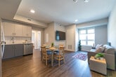 Located at 160 Sherwood Forest Square in London, Ontario, this thoughtfully designed three-bedroom, one-bathroom unit offers a functional and modern living experience across a single floor. The open-concept living and dining area serves as the heart of the home, featuring warm hardwood-style flooring, neutral grey walls, and recessed lighting. A wall-mounted television anchors the living space, while a dining table for four sits adjacent, creating a seamless flow ideal for everyday living. Natural light filters in through a window overlooking the surrounding neighbourhood, adding brightness to the shared space. The kitchen is well-appointed with two-tone grey and white cabinetry, white tile backsplash, light countertops, and a full suite of stainless steel appliances including a refrigerator, electric range, over-the-range microwave, and dishwasher. Each of the three bedrooms features hardwood-style flooring, large windows that bring in ample natural light, and individual wardrobe storage. One bedroom includes a dedicated desk area, making it well-suited for study or remote work. The shared bathroom offers a glass-enclosed stand-up shower with white tile surround and a vanity with a white countertop. A hallway laundry area houses a stacked washer and dryer unit, adding everyday convenience to this well-organized home.