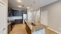 Located at 2120 N Brevard St in Charlotte, NC, this well-appointed 2-bedroom, 2-bathroom residence offers a thoughtfully designed single-level layout with modern finishes throughout. The kitchen serves as a central highlight, featuring dark espresso cabinetry, granite countertops, a large center island with a double undermount sink, stylish pendant lighting, and a full suite of stainless steel appliances, including a French door refrigerator, electric range, and built-in microwave. Light wood-style flooring flows through the kitchen and main living areas, lending a clean, contemporary feel. Both bedrooms are carpeted and bathed in natural light from large windows with views of the surrounding community. Each room offers a comfortable, versatile footprint with easy closet access. Two well-designed closets provide generous storage, including wire shelving systems for organization. The bathrooms are finished with granite-topped dark wood vanities and light wood-style tile flooring. The primary bath features a walk-in shower with classic subway tile, while the secondary bath includes a tub-shower combo with matching subway tile surround. Neutral gray tones throughout create a calm, cohesive ambiance ideal for modern urban living.