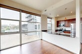 This thoughtfully designed 2-bedroom, 1-bathroom residence offers a generous floor plan spread across a single level. The open-concept living, dining, and kitchen area serves as the heart of the home, bathed in natural light through expansive floor-to-ceiling windows that frame striking urban skyline views. Rich hardwood flooring flows throughout the main living areas, adding warmth to the contemporary aesthetic.

The kitchen is well-equipped with rich wood cabinetry, dark granite countertops, stainless steel appliances including a range and refrigerator, and pendant lighting overhead. A breakfast bar provides additional prep and dining space. A sliding glass door from the living area opens to a private balcony, offering elevated city views.

The spacious primary bedroom features large floor-to-ceiling windows that continue the urban panorama, with plush carpeting for comfort. The second bedroom is equally well-lit with hardwood flooring and wall-mounted lighting. The full bathroom includes a single vanity with wood cabinetry, a tub-shower combination, and tile flooring.

Additional highlights include a dedicated in-unit laundry room, two closets for ample storage, and two hallways connecting the layout efficiently. The overall ambiance is modern, bright, and urban.