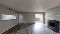 This two-bedroom, two-bathroom apartment in Arlington, Texas offers a well-organized single-level layout designed for comfortable everyday living. Dark hardwood-style flooring runs throughout the unit, creating a cohesive and modern aesthetic against neutral gray walls. The living room serves as the heart of the home, highlighted by a wood-burning fireplace with a classic white mantle and black tile surround. Sliding glass doors lead directly to a private balcony, filling the space with natural light and providing outdoor access. The kitchen features a pass-through window that connects to the living area, enhancing the open feel of the shared spaces. Both bedrooms are equipped with ceiling fans and dedicated closets — each closet outfitted with built-in shelving and hanging rods for ample storage. The primary bedroom is generously sized and includes its own private bathroom access. A second full bathroom serves the remaining bedroom and guests. Each bathroom includes a tiled tub-shower combination. A connecting hallway efficiently links all rooms, while a textured ceiling treatment is consistent throughout the unit, adding a classic residential touch to the overall design.