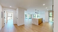 Located on North Palm Drive in the heart of Beverly Hills, this thoughtfully designed residence offers a seamless blend of modern architecture and high-end finishes. The open-concept kitchen and living area serves as the centerpiece of the home, anchored by a striking marble-clad island with warm wood accents and pendant lighting. The kitchen extends along a full wall of custom natural wood cabinetry, white marble countertops, and stainless steel appliances, all bathed in natural light from large black-framed windows overlooking lush greenery. Light oak hardwood flooring flows throughout the entire space, enhancing the bright and airy atmosphere created by recessed lighting and clean white walls. The spacious primary bedroom features floor-to-ceiling windows and a glass-railed balcony with sweeping views of Beverly Hills' iconic tree-lined streets. A generously sized walk-in closet with custom built-in shelving and drawers provides ample storage. The bathrooms are finished with dramatic marble slab walls and glass-enclosed showers, exuding a spa-like quality. The tray ceilings throughout add architectural depth, while the overall design maintains a crisp, contemporary elegance befitting its prestigious Beverly Hills address.