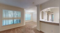 This single-floor residence offers a thoughtfully designed layout with a blend of classic architectural details and modern finishes throughout. The open living and dining area is defined by decorative columns, arched pass-through details, and crown molding, all complemented by plush wall-to-wall carpeting and multiple windows dressed with horizontal blinds that invite generous natural light. A pendant light fixture anchors the dining space, adding a refined touch.

The kitchen is well-equipped, featuring stainless steel appliances including a refrigerator, range, over-the-range microwave, and dishwasher. White shaker-style cabinetry pairs with granite countertops and a light tile backsplash, while hardwood-style flooring adds warmth underfoot. A pass-through counter connects the kitchen to the living area for seamless flow.

The bedrooms are generously sized, each featuring plush carpeting, ceiling fans, crown molding, and windows overlooking lush greenery. Closet space is provided, including a walk-in option in the primary bedroom. The primary bathroom is spacious, offering a soaking tub, a separate arched glass-enclosed shower, a vanity with granite countertops, and large mirrors. A secondary bathroom provides a classic tub-shower combination with clean white tile finishes throughout.