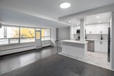 Located at 155 Balliol Street in Toronto's Davisville Village neighbourhood, Unit 314 is a single-floor residence featuring a thoughtfully renovated interior with a clean, modern aesthetic. The open-concept kitchen has been fully updated with crisp white cabinetry extending to the ceiling, a marble-style tile floor, stone-finish countertops, a subway tile backsplash, and a full suite of stainless steel appliances including a refrigerator, dishwasher, and range with microwave. A peninsula with a waterfall-edge counter connects the kitchen to the living areas, providing additional prep and seating space.

The living and dining areas are defined by herringbone-patterned parquet flooring in a grey tone, carried consistently throughout the unit. A split-level layout adds architectural interest, with steps separating distinct zones within the main living space. Large floor-to-ceiling windows allow generous natural light to fill the room while framing views of the surrounding Midtown Toronto streetscape and autumn foliage. A wall-mounted air conditioning unit and baseboard heating provide year-round climate control.

The bedrooms are quiet and functional, featuring the same parquet flooring, neutral walls, and ample closet space with double-door configurations. The overall palette is neutral and understated, creating a clean, move-in ready environment.