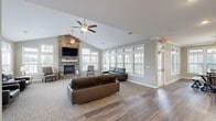 Located at 890 Quail Creek Blvd in Stow, Ohio, this single-floor community space offers a thoughtfully designed layout that combines comfort and functionality. The welcoming entrance greets visitors with crown molding details, warm neutral tones, hardwood-style flooring, and a decorative round mirror above a console table, setting an inviting tone throughout.

The expansive living room is a standout feature, highlighted by soaring vaulted ceilings, a dramatic floor-to-ceiling stacked stone fireplace with a wall-mounted television, and an abundance of natural light streaming through multiple double-hung windows with transom accents. Ceiling fans provide year-round comfort. The carpeted seating area accommodates generous lounge furniture, creating a relaxed gathering atmosphere.

The open-concept dining area flows naturally from the living room and features hardwood-style flooring, large windows offering outdoor views, a pendant chandelier, and a stone-accented kitchen island with a light countertop. The kitchen is equipped with white shaker cabinetry, dark granite countertops, stainless steel appliances, a double sink, and crown molding — practical yet polished.

Throughout, the consistent use of soft gray walls, white trim, and natural light creates a cohesive, bright, and welcoming ambiance ideal for community gatherings.