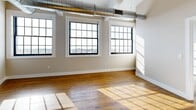 Located at 2075 Kenmore Ave in Buffalo, NY, this 2-bedroom, 2-bathroom unit showcases a compelling blend of industrial character and modern finishes. Soaring ceilings with exposed structural beams and silver ductwork run throughout, lending an authentic loft aesthetic to the space. Rich hardwood floors extend across every room, reflecting natural light that pours in through large, multi-pane factory-style windows.

The open-concept kitchen and living area serves as the heart of the unit. The kitchen is outfitted with white shaker cabinetry, granite countertops, a center island with an undermount sink, and a full suite of stainless steel appliances including a refrigerator, range, microwave, and dishwasher. Striking industrial pendant lights hang overhead, complementing the high ceilings.

The bedrooms are generously proportioned, each bathed in natural light from large windows with exterior views. The primary bedroom features a set of French doors, adding an elegant touch. Both bathrooms are cleanly appointed — one with a granite-topped white vanity and mirrored medicine cabinet, the other with a full soaking tub, built-in shelving, and tile flooring. A dedicated closet provides additional storage, completing this well-designed urban residence.