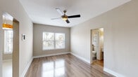 Located at 3715 W 1st St in the heart of Los Angeles, CA, this single-floor unit offers a clean, modern aesthetic with a practical and well-organized layout. Throughout the main living areas, warm wood-look flooring adds a polished, cohesive feel, while neutral beige walls create a bright and inviting atmosphere. The living area is spacious and airy, featuring a ceiling fan with integrated lighting and a window fitted with blinds that frames views of the surrounding neighborhood, allowing natural light to fill the room. A solid white entry door provides a welcoming focal point near the front of the space. The kitchen is efficiently designed with a galley-style layout, featuring white cabinetry, stainless steel appliances including a gas range and full-size refrigerator, and light tile flooring, offering both functionality and a contemporary look. The bedroom is generously sized, with its own ceiling fan and a window overlooking the outdoors. It connects seamlessly to a dressing area complete with a built-in white vanity featuring multiple drawers, a wall-mounted mirror, and sconce lighting, alongside an open closet for ample storage. The bathroom is neatly appointed with large-format grey tile flooring, a white vanity with an undermount sink, and a shower/tub combination enclosed by sliding glass doors, with a window above providing natural ventilation.