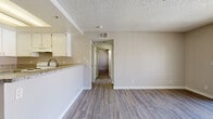Located at 18215 Foothill Blvd in Fontana, CA, this 2-bedroom, 2-bathroom unit offers a practical and well-appointed single-floor layout. Wood-look laminate flooring runs throughout, providing a cohesive and easy-to-maintain surface across every room. The combined kitchen and living room serves as the heart of the unit, where white cabinetry, granite-style countertops, and a stainless steel sink give the kitchen a clean, functional feel. A white electric range and ample cabinet storage complete the cooking space. A breakfast bar-style counter opens the kitchen toward the living area, which is brightened by a ceiling fan and a sliding glass door that invites natural light and outdoor access. A central hallway connects the living spaces to the two bedrooms and bathrooms. Each bedroom features neutral-toned walls, wood-look flooring, textured ceilings, and windows fitted with vertical blinds for light control and privacy. The two bathrooms are finished with granite-top vanities, white cabinetry, and wood-look flooring — one featuring a shower-tub combination. Two closets provide additional storage. The overall palette of soft neutrals and white trim lends the space a clean, move-in-ready character.