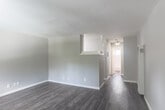 Located at 902 W Remington Dr in Sunnyvale, California, this single-floor, one-bedroom, one-bathroom residence offers a thoughtfully laid-out living space with clean, neutral finishes throughout. The living room is an open, airy space featuring durable wood-look flooring in a warm gray-brown tone and soft gray walls that lend a calm, modern ambiance. Natural light filters into the room, complementing the understated palette. A half-wall pass-through seamlessly connects the living area to the kitchen, promoting an open feel while maintaining a defined layout. The kitchen is equipped with a white coil-top range and cabinetry, offering a practical and efficient cooking space. A hallway leads from the main living area to the private bedroom, which features plush carpeting, a window with blinds that invites natural light, and two closets providing generous storage. The bathroom includes a full tub-shower combination with white tile surround and a frosted window for privacy and ventilation. A wall-mounted heating unit in the living room ensures year-round comfort. Two additional closets throughout the unit add to the overall storage functionality of this well-appointed Sunnyvale residence.