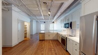 Located at 2901 Rosewood Dr in Columbia, SC, this single-floor space showcases a compelling blend of industrial character and contemporary refinement. The soaring ceilings feature exposed white-painted steel trusses and open ductwork, lending the interior a loft-like openness that is both functional and visually striking. Warm hardwood flooring runs throughout, tying together the various areas with a cohesive, inviting aesthetic.

The expansive kitchen is a standout feature, equipped with soft gray shaker-style cabinetry, quartz countertops, a subway tile backsplash, and a full suite of stainless steel appliances including a range, microwave, dishwasher, and refrigerator. A generous island with a built-in sink and pendant lighting overhead adds both workspace and visual focus to the open layout.

Multiple open rooms with painted cinder block or shiplap walls and large, light-filtering windows offer flexible use potential. Track lighting supplements natural light throughout, ensuring brightness across the entire floor plan.

The bathrooms are finished to a high standard, featuring marble-look porcelain tile on both the floors and shower surround, dark quartz vanity countertops, undermount sinks, and sleek matte black hardware — delivering a clean, modern aesthetic throughout.