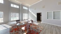 This single-floor space is defined by its dramatically tall ceilings and an open, airy layout that immediately conveys a sense of grandeur. Crisp gray walls, crown molding, and light wood-tone flooring run throughout, creating a cohesive and contemporary aesthetic.

The main gathering area is generously proportioned, anchored by a tile-surround fireplace flanked by built-in shelving and cabinetry on either side—a functional and visually striking focal point. Natural light pours in abundantly through a combination of large lower windows and elevated transom windows positioned high along the walls, casting long, dramatic streaks of sunlight across the floors throughout the day.

The seating area is furnished with modern mid-century-influenced chairs, glass-top accent tables with gold frames, a loveseat, and a vibrant patterned area rug in rich reds and grays, adding warmth and color to the otherwise neutral palette.

A set of glass-paned exterior doors provides direct access to the outdoors, reinforcing the space's connection to the surrounding environment. Additional areas branch off from the main room, including what appears to be a secondary workspace or office area. Overall, the space offers a welcoming, well-lit, and thoughtfully designed environment suited for gathering and collaboration.
