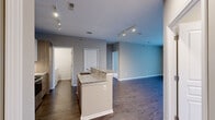 This single-floor residence is designed with a practical open-concept layout that connects the kitchen and living areas seamlessly. The kitchen serves as a central hub, anchored by a peninsula island topped with granite countertops that provides both additional workspace and a natural dividing point between the cooking and living areas. White upper cabinetry is paired with wood-toned lower cabinets and drawers, complemented by stainless steel appliances including a refrigerator, range, and built-in microwave. Track lighting illuminates the kitchen and open living space, which features dark hardwood-style flooring throughout.

The living area extends to a sliding glass door that opens onto a private balcony offering outdoor views. Bedrooms feature soft carpeting and corner windows that allow natural light, while ample closet storage is provided by bifold doors. The primary bathroom includes a sleek double-vanity with vessel sinks, a wide mirror, wood-look flooring, and a separate glass-enclosed shower. A secondary bathroom offers a full tub-shower combination. A dedicated laundry room houses a full-sized washer and dryer alongside a water heater, adding everyday convenience to the unit.