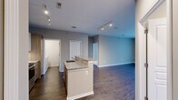 This single-floor residence is designed with a practical open-concept layout that connects the kitchen and living areas seamlessly. The kitchen serves as a central hub, anchored by a peninsula island topped with granite countertops that provides both additional workspace and a natural dividing point between the cooking and living areas. White upper cabinetry is paired with wood-toned lower cabinets and drawers, complemented by stainless steel appliances including a refrigerator, range, and built-in microwave. Track lighting illuminates the kitchen and open living space, which features dark hardwood-style flooring throughout.

The living area extends to a sliding glass door that opens onto a private balcony offering outdoor views. Bedrooms feature soft carpeting and corner windows that allow natural light, while ample closet storage is provided by bifold doors. The primary bathroom includes a sleek double-vanity with vessel sinks, a wide mirror, wood-look flooring, and a separate glass-enclosed shower. A secondary bathroom offers a full tub-shower combination. A dedicated laundry room houses a full-sized washer and dryer alongside a water heater, adding everyday convenience to the unit.
