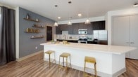 This well-appointed 1-bedroom, 1-bathroom residence offers a cohesive and modern living experience across a single floor. The open-concept kitchen is a standout feature, showcasing dark espresso cabinetry, white quartz countertops, a classic subway tile backsplash, and stainless steel appliances including a refrigerator with ice maker, range, and microwave. A generous breakfast bar with pendant lighting provides casual seating and separates the kitchen from the living area. Rustic floating wood shelves add a warm, decorative accent to the kitchen wall. The living room is bright and welcoming, featuring large windows with abundant natural light, wood-look flooring, and an eye-catching patterned accent wall that adds personality to the space. The bedroom is spacious and comfortable, highlighted by a bold navy accent wall, plush carpeting, a ceiling fan, and French doors that open to an outdoor area, allowing natural light to pour in. The full bathroom is clean and functional, featuring matching dark cabinetry, white quartz countertops, a large vanity mirror, wood-look flooring, and a tub-shower combination. Consistent design elements—including dark cabinetry and wood-look flooring—create a unified, contemporary aesthetic throughout the residence.