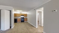 This single-floor, two-bedroom unit offers a practical and comfortable layout with wood-style flooring carried consistently throughout the living spaces. The open living area is bright and spacious, featuring a sliding glass door that provides direct access to an outdoor area and allows natural light to fill the room. The kitchen is efficiently designed in an L-shaped configuration, outfitted with warm honey-toned wood cabinetry, laminate countertops, and a full suite of black appliances including a refrigerator, electric range, dishwasher, and a double-basin sink. Upper transom windows in the kitchen add additional natural light. The bedrooms are well-proportioned, each featuring wood-style flooring and ceiling fans with integrated lighting. One bedroom includes an expansive wall of built-in closet space with bifold doors, offering ample storage capacity. The bathroom is equipped with a full-size soaking tub and shower combination with white surround walls, a toilet, and a towel bar. Neutral gray walls, white trim, and textured ceilings provide a clean, cohesive aesthetic throughout the entire unit.