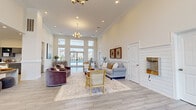 Located along 101st Airborne Division Parkway in Clarksville, Tennessee, this single-story community space offers a well-appointed, light-filled environment designed for both functionality and comfort. The layout encompasses a spacious main lounge, a private office, and a kitchenette area, all unified by consistent light wood-look tile flooring and a neutral warm-white color palette throughout.

The main lounge is the centerpiece of the space, boasting soaring ceilings adorned with crown molding, recessed lighting, and an elegant chandelier. Oversized windows and glass entry doors flood the area with natural light and provide views toward an outdoor pool. The open layout accommodates multiple seating arrangements, creating a welcoming and social atmosphere.

Adjacent to the lounge, a kitchenette features slate-blue cabinetry with open shelving, a white subway tile backsplash, quartz countertops, a double stainless steel sink, and stainless steel appliances. A pair of cream accent chairs nearby adds a comfortable lounge element to this functional area.

The private office is a quieter, well-proportioned room with chair-rail wainscoting, a ceiling fan, natural light from large windows, and a wood desk with guest seating—ideal for consultations or administrative tasks.

A secondary entry area near the front provides additional natural light through floor-to-ceiling windows, contributing to the overall bright and airy ambiance of the space.