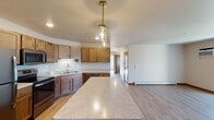 This single-floor residence offers a thoughtfully designed layout that balances functionality and comfort throughout its interconnected spaces. The kitchen serves as a central highlight, featuring warm-toned wood cabinetry, light marble-style countertops, and a full suite of stainless steel appliances including a refrigerator, electric range, built-in microwave, and dishwasher. A peninsula with matching countertop provides additional workspace and a pendant light fixture adds a decorative touch overhead. Light hardwood flooring runs throughout the kitchen and living areas, lending a cohesive, clean aesthetic.

The open living area benefits from natural light through a sliding glass door that connects to an outdoor area, as well as additional windows with views of surrounding greenery. Baseboard heating is present throughout, supplemented by wall-mounted air conditioning units for year-round climate control.

The bedrooms feature plush carpeting, ceiling fans with lighting, and windows that invite natural light. Two bathrooms serve the unit: one with a soaking tub and shower combination and marble-style countertops, and a second with a standalone walk-in shower. Both bathrooms include light hardwood-style flooring and vanity storage, completing this practical and well-finished space.