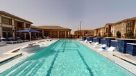 Located at 20220 Bellaire Blvd in Richmond, TX, this single-story community amenity center offers residents a well-rounded collection of shared facilities designed for comfort and recreation. The outdoor centerpiece is a generously sized, resort-style swimming pool with crystal-clear turquoise water, lined with sleek modern loungers and shaded seating areas beneath umbrellas. The pool deck provides a relaxed atmosphere with views of the surrounding residential buildings. Inside, the clubhouse is accessed through elegant glass-paned French doors that hint at the refined interior beyond. The interior features warm hardwood-style flooring, a tastefully decorated lounge area with contemporary furnishings, and a chandelier that adds a touch of sophistication. Neutral gray walls are accented with framed botanical artwork, contributing to a calm and welcoming ambiance throughout. A dedicated fitness center is visible through interior windows, equipped with cardio machines and a large ceiling fan, ensuring a well-ventilated workout environment. Safety features such as fire alarm systems are integrated throughout the building. The overall design blends modern aesthetics with functional community living, creating an inviting space for residents to relax, socialize, and stay active.