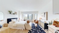Located at 166 Van Reipen Avenue in Jersey City, NJ, this one-bedroom, one-bathroom residence offers a thoughtfully designed layout spread across a single floor. The open-plan living and kitchen area forms the heart of the unit, featuring light oak hardwood flooring, crisp white walls, and an abundance of natural light that creates a bright, airy atmosphere. The kitchen is equipped with stainless steel appliances, light wood cabinetry with open shelving, and a clean subway tile backsplash, seamlessly integrating with the living space. The generously proportioned bedroom accommodates a full furniture arrangement with ease, showcasing the same warm hardwood flooring, a dedicated vanity area, and a wall-mounted display shelf, lending the room a refined yet comfortable character. A dedicated walk-in closet adjoins the bedroom, offering wrap-around hanging rails and ample storage space with light wood flooring throughout. The bathroom is finished in neutral tones with large-format floor tiles, a glass-enclosed shower, and clean white fixtures, maintaining the unit's consistent modern aesthetic. A hallway connects the key areas of the residence, completing a practical and well-organized floor plan. The overall design palette — warm woods, whites, and soft neutrals — creates a cohesive and welcoming living environment.