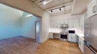 Located at 2901 Rosewood Dr in Columbia, SC's vibrant Rosewood neighborhood, this single-floor space blends industrial character with modern renovations. The kitchen serves as a standout feature, showcasing light gray shaker-style cabinetry extending to the ceiling, white quartz countertops, a classic subway tile backsplash, and a full suite of stainless steel appliances including a range, dishwasher, refrigerator, and microwave. Exposed metal trusses and track lighting overhead reinforce the space's industrial aesthetic. Warm hardwood flooring runs throughout the main living and sleeping areas, creating a cohesive and inviting atmosphere. Multiple rooms feature dramatically vaulted ceilings with exposed wooden rafters and painted shiplap, lending a distinctive architectural character. Painted concrete block walls in select areas add to the raw, loft-inspired feel. The bathrooms are finished with large-format marble-look porcelain tile flooring, white cabinetry with black hardware, and glass-enclosed showers, offering a clean and contemporary contrast to the industrial elements. A walk-in closet provides practical storage. The overall design balances rugged structural elements with refined modern finishes, making this a versatile and visually compelling space.