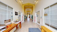 This single-floor community clubhouse at 3770 W 24th St in Greeley, Colorado offers residents a well-rounded collection of amenity spaces spanning a generous footprint. The heart of the clubhouse is a spacious lounge area featuring soaring ceilings, warm yellow walls, tile flooring with decorative area rugs, and a striking full-height stacked-stone fireplace flanked by large windows and glass doors that invite natural light and provide views of the outdoor pool area. Adjacent to the lounge, a fully equipped kitchen includes ample wood cabinetry, a double sink, countertop appliances, and a stainless steel prep station, supporting community gatherings and events. The exercise room is bright and well-lit by large windows, and is outfitted with cardio equipment including a treadmill, elliptical, and stationary bike, along with free weights and a Precor multi-station strength machine. Wall-mounted mirrors enhance the sense of space. A dedicated kids' area and library room features tile flooring, a patterned area rug, a children's table and chairs, a bookshelf, and direct outdoor access via a glass-paneled door. Two office spaces and four hallways complete the interior layout. Outdoors, a large swimming pool is surrounded by a spacious deck with seating, set within a landscaped courtyard framed by the surrounding residential buildings.