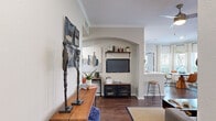 This single-story residence offers a thoughtfully designed layout across two bedrooms and three bathrooms. The open-concept living, dining, and kitchen area forms the heart of the home, anchored by rich hardwood-style flooring and crown molding details. The living room features a distinctive arched alcove housing a wall-mounted television, complemented by a long wooden console and curated artwork. Natural light fills the dining area through multiple windows dressed with plantation shutters and sheer curtains, framing outdoor greenery views around a rounded wood dining table.

The galley-style kitchen is equipped with stainless steel appliances, white upper cabinetry, gray lower cabinets, quartz countertops, and a tile backsplash. A dedicated laundry room with wire shelving provides added convenience. A central hallway connects both bedrooms, each finished with plush carpet and windows with outdoor views. The primary bedroom offers a ceiling fan and ample natural light. Both bedrooms reflect a calm, neutral palette. Three full bathrooms serve the layout efficiently. Throughout the residence, a cohesive blend of warm wood tones, neutral walls, and contemporary fixtures creates a refined, comfortable ambiance.