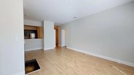 Located at 757 Saltmeadow Bay Dr in Virginia Beach, Virginia, this single-floor residence offers a clean, modern aesthetic throughout. The open-concept living area is anchored by light-toned hardwood flooring that extends seamlessly throughout the main living space, creating a warm and inviting atmosphere. Neutral gray walls and crisp white trim and baseboards contribute to a bright, contemporary feel that pairs well with the natural tones of the flooring.

The kitchen is partially open to the living area, separated by a countertop bar that provides both a functional workspace and a casual dining surface. Dark cabinetry contrasts with the lighter countertops, while a stainless steel refrigerator adds a modern touch to the culinary space. The layout allows for easy interaction between the kitchen and the main living area, making it well-suited for everyday living and entertaining.

A hallway visible from the living area leads to additional rooms, suggesting a practical and well-organized floor plan. Recessed lighting and ceiling vents are integrated into the smooth white ceiling, ensuring comfortable climate control throughout. The overall design of the space emphasizes simplicity, functionality, and a cohesive neutral palette that offers a versatile canvas for a variety of interior styles.