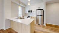 Located at 660 Sunningdale Rd E in London, Ontario, this well-appointed one-bedroom unit offers a thoughtfully designed single-floor layout with a clean, contemporary aesthetic. Light hardwood flooring runs throughout the space, creating a warm and cohesive look from room to room.

The open-concept kitchen and living area forms the heart of the unit. The kitchen is outfitted with white upper cabinetry, natural wood-toned lower cabinets, and stainless steel appliances, including a full-sized refrigerator, electric range, and over-the-range microwave. A peninsula with a white countertop and double sink provides both additional prep space and a casual dining option, while pendant lighting overhead adds a polished finishing touch. A window in the kitchen allows natural light to brighten the workspace.

The living area is generously proportioned, featuring tall, narrow windows that fill the room with natural light and provide open outdoor views of the surrounding landscape.

The bedroom is a comfortable, private retreat with a large sliding glass door leading to a private balcony, offering elevated views of greenery and water. Two closets provide ample storage throughout the unit.

A dedicated laundry area with built-in cabinetry, a sink, and a tall window completes this functional and modern space.